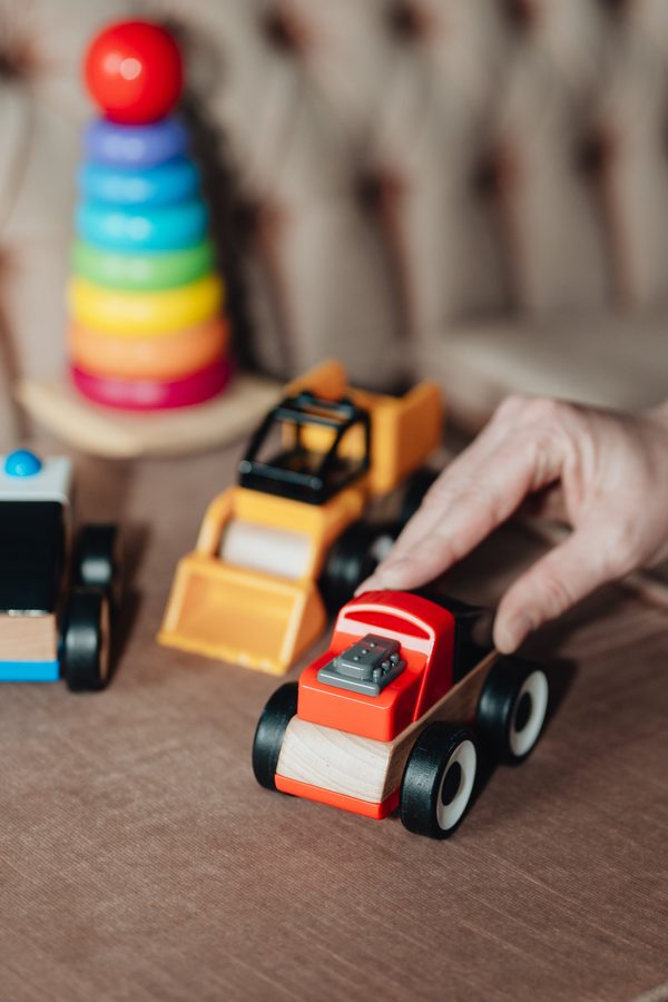 A hand with wooden toy cars and a rainbow stacker